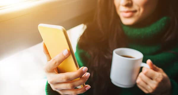 young-brunette-woman-sits-windowsill-holding-smartphone-cup-tea